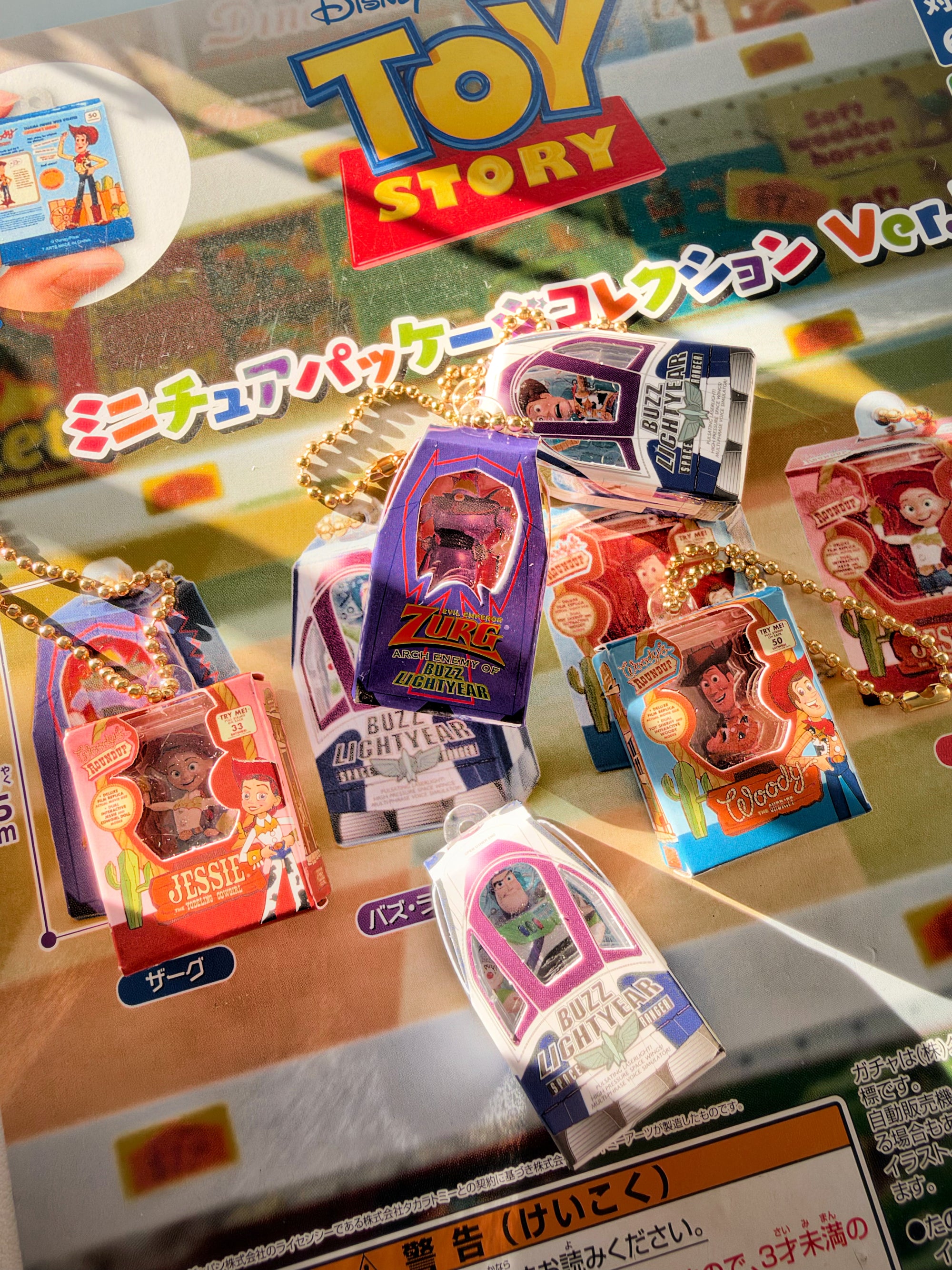 A close-up of several small Toy Story-themed keychain packs and charms arranged on a printed display card. The packaging features colorful character art and Japanese text, with visible Toy Story branding at the top.